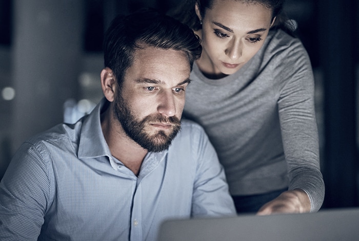 woman looking over mans shoulder on laptop